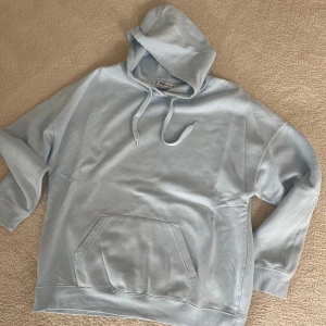 Ljusblå hoodie från FAS - Säljer en supermjuk och bekväm ljusblå hoodie. Den har en klassisk känguruficka och justerbar huva med dragsko. Perfekt för en avslappnad stil eller mysiga dagar hemma. Passar bra till både jeans och mjukisbyxor!