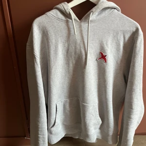 Grå hoodie från Axel Arigato - Snygg grå hoodie från Axel Arigato med en röd broderad fågel på bröstet. Tröjan har en klassisk känguruficka och justerbar huva med dragsko. Nypris 2000 kr så till detta pris och skick är det ett kap. Knappt använd, säljes pga för liten för mig