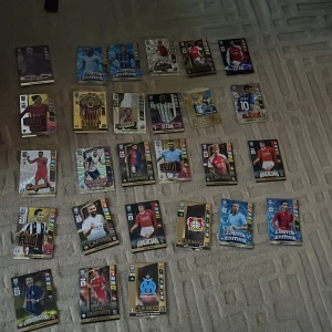 Samling av fotbollskort med olika spelare och klubbar - En samling av fotbollskort med olika spelare och klubbar. Kort med titlar som 'Titan', 'Captain', 'Magic Man' och 'Club Badge'. Innehåller kort i olika färger och design, inklusive guld och blå metallic. Korten på bilden har en sammanlagt värde på 1500+ om man vill sälja vidare. Pris kan diskuteras