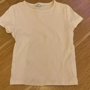 Beige ribbad t-shirt från Kappahl  - Säljer en stilren beige ribbad t-shirt från Monki. Den har en klassisk rund hals och korta ärmar, perfekt för en avslappnad look.