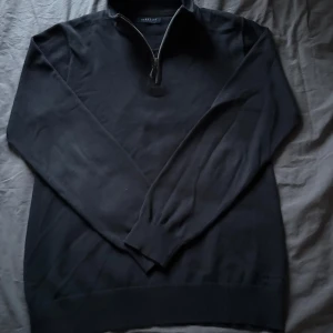 Mörkblå tröja med halfzip från Berkeley - Snygg mörkblå tröja från Berkeley med dragkedja vid halsen. Perfekt för kyligare dagar med sin långärmade design och ribbade detaljer vid ärmslut och nederkant. Den är ganska liten i storlek och nypris ligger på drygt 1300kr.