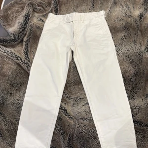 Vita byxor från Oscar Jacobson - Snygga vita byxor från Oscar Jacobson, perfekta för en stilren look. Byxorna har en klassisk design med midwaist och raka ben. Tillverkade i ett bekvämt material som passar både till vardags och mer formella tillfällen. Använd en gång till förra årets student mottagningar, ny pris 1600. 