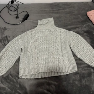 Grå stickad polotröja - Säljer en mysig grå stickad polotröja med flätmönster. Tröjan har långa ärmar och en hög krage som håller dig varm under kyliga dagar. Perfekt för höst och vinter! Använd lite 