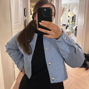 Ljusblå boucléjacka med knappar - Säljer en stilren ljusblå boucléjacka från H&M. Jackan har en croppad passform och har silvriga knappar framtill. Aldrig använd.