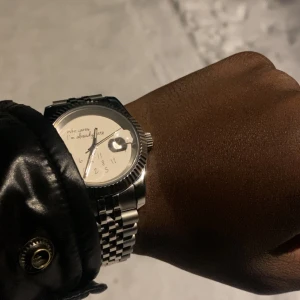 Seiko mod - Stilren silverfärgad klocka med ett unikt urtavla där det står 'Who cares I'm already late'. Klockan har en klassisk länkarmband och en tydlig datumvisare. Perfekt för den som vill ha en humoristisk touch på sin stil.