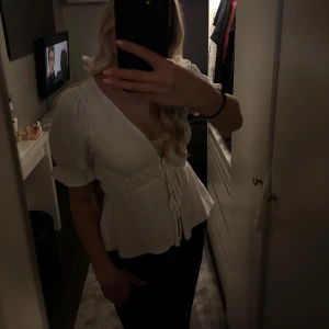 Vit blus från Gina Tricot - Säljer en söt vit blus från Gina Tricot med puffiga kortärmar och knytning i midjan. Blusen har en djup v-ringning och är tillverkad i ett lätt och luftigt material. 