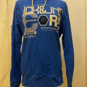 Blå hoodie från Jack & Jones M - Säljer en blå hoodie från Jack & Jones med tryck framtill.  Längd: 71 cm Armhåla till armhåla: 51 cm  Inga bilder när den sitter på mig! Katter finns i hemmet