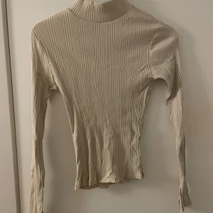 Beige ribbad polotröja - Beige tröja med turtleneck från Gina! Slits i ärmarna