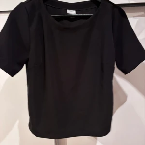 Svart blus från Jacqueline - Elegant svart blus med korta ärmar och rund halsringning. Perfekt för både vardag och mer formella tillfällen. Något stor i storleken. 