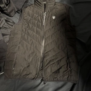 Svart quiltad väst från Emporio Armani - Snygg svart quiltad väst från Emporio Armani med dragkedja och logotypdetalj på bröstet. Perfekt för lager-på-lager under kyliga dagar. Pris kan diskuteras 