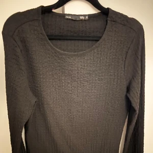 Svart ribbad tröja - Snygg svart ribbad tröja med långärmad design. Perfekt för lager-på-lager eller som en stilren baströja. Den har en rund halsringning och är tillverkad i ett bekvämt material.