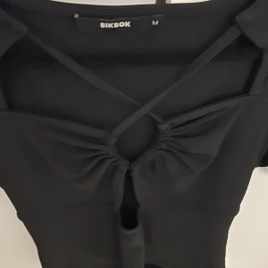 Svart topp från BikBok - Snygg svart topp från BikBok med korta ärmar och en unik snörningsdetalj framtill. Toppen har en croppad passform och är perfekt för en trendig look.