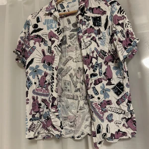 Mönstrad skjorta från NIKBEN - Cool skjorta från NIKBEN med ett färgglatt och lekfullt mönster i lila, blått och svart på vit bakgrund. Skjortan har korta ärmar och knappar framtill. Perfekt för en avslappnad stil.