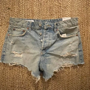 Ljusa jeansshorts med slitningar från zara  - Snygga ljusa jeansshorts från zara med slitna detaljer och fransiga kanter i storlek 38. De är aldrig använda och har även alla lappar kvar från när de köptes. De har en klassisk femficksdesign och knappar. Säljer pga att jag köpte dem online men de inte passade och jag ej kunde skicka tillbaka. Original pris 329kr