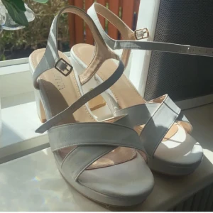 Vita klackskor  - Eleganta vita klackskor och justerbara remmar. Perfekta för sommarens festligheter med en stilren design och bekväm passform.