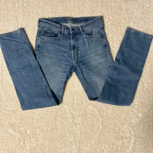 Blå jeans från Dressmann - Snygga blå jeans från Dressmann i regular fit. Klassisk design med fem fickor och knappgylf. Perfekta för en avslappnad stil.