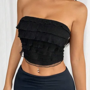 Svart tubtopp  - Snygg svart tubtopp med flera lager av volanger. Perfekt för en kväll ute eller en fest. Toppen är axelbandslös och har en croppad passform.