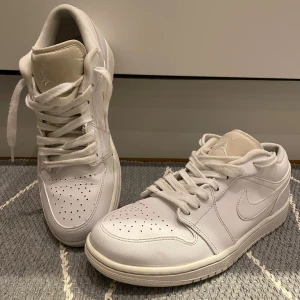 Nike Air Jordan  - Säljer ett par vita Nike Air Jordans med klassisk design och snörning. Skorna har en stilren look med perforerade detaljer på tån och en broderad logga på hälen.  De är i begagnat skick och har ett litet hål i hälen inuti ena skon (se bild). Finns inga andra hål eller separationer.