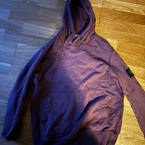 Vinröd hoodie från Stone Island - Säljer en snygg vinröd hoodie från Stone Island. Den har en klassisk design med huva och en praktisk magficka. Perfekt för en avslappnad stil.