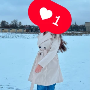 Beige trenchcoat med bälte - Snygg beige trenchcoat med knappar och bälte i midjan. Perfekt för kyliga dagar och ger en stilren look. Långärmad design som passar bra till både jeans och klänning.