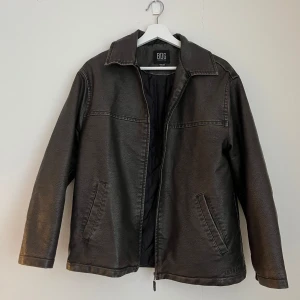 Svart skinnjacka från BDG - Knappt använd snygg jacka i konstläder från BDG, Urban outfitters. Mörkbrun. Nyskick! XXS men är oversize så tror den kan passa någon som brukar ha XS-M beroende på önskad passform.