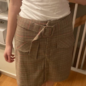 Rutig kjol med bälte - Snygg rutig kjol med vintage-look med avtagbart bälte till. Vill meddela att ”fickorna” endast är detaljer :) Stängs smidigt med knappar på framsidan! Knappt använd så är i gott skick! 🤎