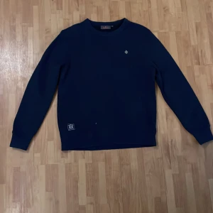 Mörkblå tröja med broderad logga - Snygg mörkblå tröja med en liten broderad logga på bröstet. Tröjan har långa ärmar och en rund halsringning. Perfekt för en stilren och avslappnad look. Märket är Morris