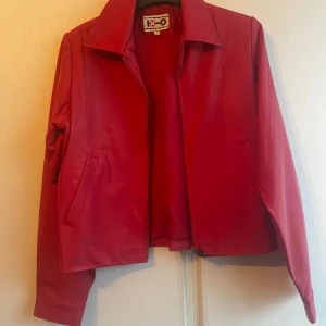 Röd jacka från IX-O - Snygg röd jacka från IX-O med dragkedja framtill och klassisk krage. Jackan har en stilren design med långa ärmar och två fickor på framsidan. Perfekt för att ge en färgklick till din outfit.