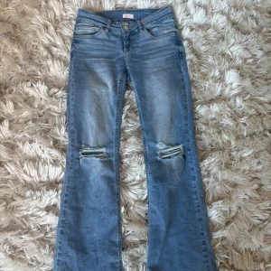 Blå bootcut jeans med hål - Snygga blå bootcut jeans med hål på knäna. Säljer pågrund av att dom inte används och inte sitter så bra på mig. De har en klassisk femficksdesign och knappgylf. De är använda fåtal ggr.💕