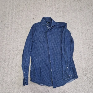 Blå mönstrad skjorta från Hugo Boss - Snygg blå skjorta från Hugo Boss med diskret mönster och slim fit passform. Skjortan är använd ett par gånger.