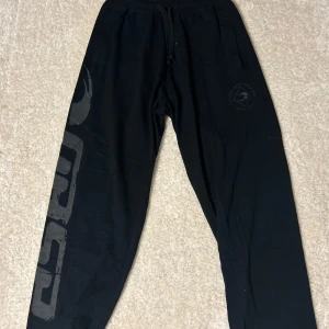 Svarta mjukisbyxor från gasp - Svarta mjukisbyxor från gasp med elastisk midja. Byxorna har en tryckt logga längs benet och är perfekta för en avslappnad stil eller gymmet .