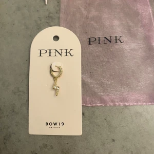 Guldörhänge med blixtberlock från BOW19 - Snyggt guldörhänge från BOW19 med en glittrig blixtberlock. Kommer med en rosa förvaringspåse. Helt oanvänd för råkat få dubbelt