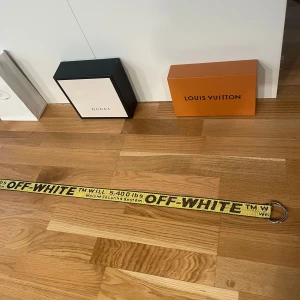 Gult bälte från Off-White - Säljer ett coolt gult bälte från Off-White med svart text och metallspänne. Perfekt för att ge din outfit en edgy touch. Bältet har en industriell design och är känt för sin unika stil.