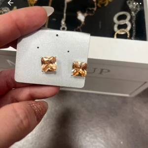 Kvadratiska örhängen med glittriga stenar - Snygga kvadratiska örhängen med stora glittriga stenar i en varm, gyllene ton. Perfekta för att ge en touch av glamour till din outfit. Lätta att bära och passar till många tillfällen.