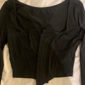 Svart långärmad korsettopp - Snygg svart korsettopp med långa ärmar och knäppning framtill. Använd en gång 