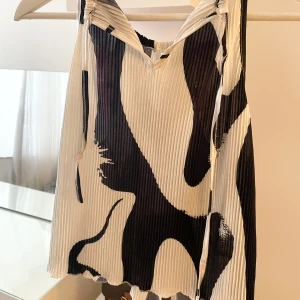 Svartvit ärmlös topp - Snygg ärmlös topp i svartvitt abstrakt mönster. Toppen har en ribbad struktur och knytband som går bakom nacken där man knyter en rosett samt går att justera. Perfekt för en sommar kväll. 