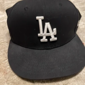 Svart keps med LA-logga - Snygg svart keps från New Era med broderad LA-logga i vitt framtill. På sidan finns ett World Series 1981-märke. Perfekt för sportiga tillfällen eller som en stilren accessoar.
