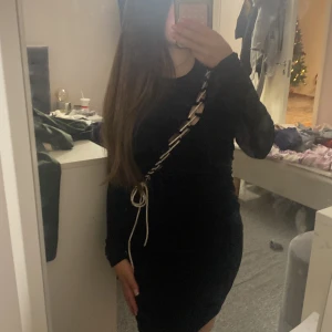 Svart klänning från FB Sister - Snygg svart klänning från FB Sister med lång ärm och unik snörningsdetalj i vitt som går diagonalt över framsidan. Perfekt för en stilren look.