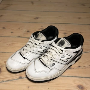 Vita New Balance 550 sneakers - Säljer ett par vita New Balance 550 sneakers med svarta detaljer. Måste tyvärr sälja skorna då de är lite för små nu men de är fortfarande i bra skick. Om du har några funderingar kring skorna är det bara att höra av dig.