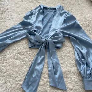 Silkes topp med öppen rygg  - En jättefin ljusblå silkes topp från NA-KD. Knyts där bak så man får en öppen fin rygg. Aldrig använd! Lapp kvar! 