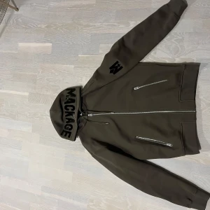 Brun/Mörk grön hoodie från Mackage - Snygg brun/Mörk grön hoodie från Mackage Stl M med dragkedja och stor logga på huvan. Tröjan har långa ärmar och två fickor med dragkedjor framtill. Perfekt för en avslappnad stil. Köpt på Johnells. Använd 2 gånger