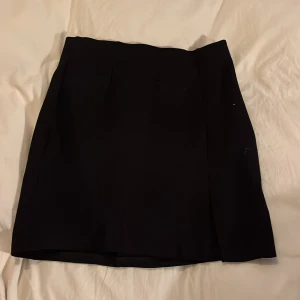 Svart kjol - Snygg svart kortkjol med en stilren design. Perfekt för en elegant look. Kjolen har en diskret slits framtill som ger extra rörelsefrihet.