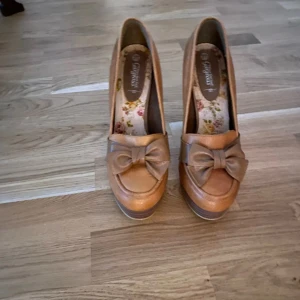 Bruna pumps med rosett - Snygga bruna pumps med hög klack och dekorativ rosett framtill. Perfekta för att ge en elegant touch till din outfit.