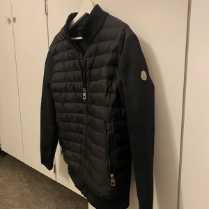 Svart quiltad jacka från Moncler - Snygg svart quiltad jacka från Moncler med dragkedja och långärmade ärmar. Perfekt för kyligare dagar med sin stilrena design och bekväma passform.