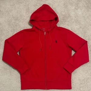 Ralph lauren zip hoodie - Snygg röd hoodie från Ralph Lauren med dragkedja med logga på bröstet. Jag köpte den på Plick för 900 men säljer eftersom den har nu legat i min garderob i ett år utan att användas. Tröjan är helt ny utan lappar som jag tog av när jag köpte. Skriv till mig vid intresse!!