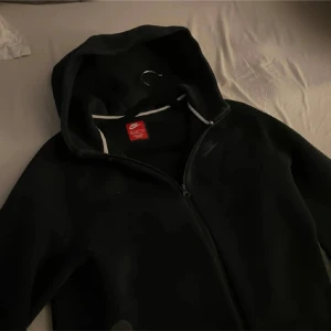 Svart hoodie från Nike/tech fleece - Säljer en svart hoodie från Nike med dragkedja och huva. Perfekt för en avslappnad stil. Den har en klassisk design med Nike-logga på bröstet.