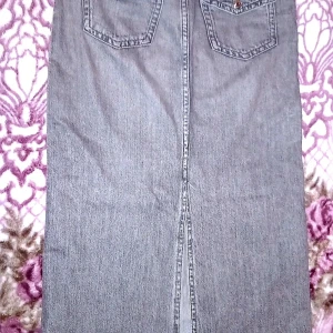 Grå jeanskjol från gina tricot young  - Snygg grå jeanskjol från gina tricot young med praktiska fickor och knappdetaljer. Kjolen har en klassisk design med en slits baktill för extra rörelsefrihet. Perfekt för en avslappnad stil.