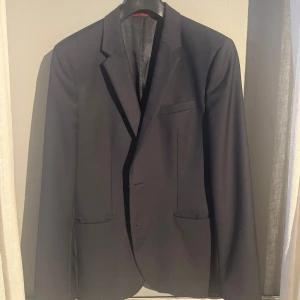 Hugo Boss kavaj - Elegant svart kavaj från Hugo Boss som jag ägt i 6 månader. Nypris är cirka 3000kr.Kostymen är i nyskick och storlek 50 ,som defineras till storlek S-M. Frågor så är de bara att höra av sig mvh Albin😁