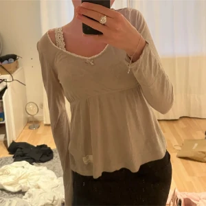 Beige långärmad topp från Odd Molly - Säljer en söt beige långärmad topp från Odd Molly med spetsdetaljer vid halsringningen och en liten rosett framtill. Köpt på plick! Toppen har en avslappnad passform och ett fint märke på ärmen. Perfekt för en avslappnad stil.