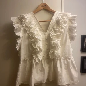 Vit blus med volangdetaljer - Säljer en söt vit blus med volangdetaljer och v-ringning💗 Nypris 919 kr